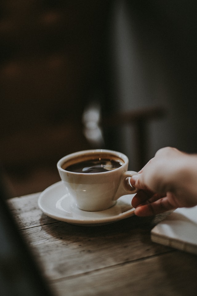 tangan sedang menggenggam secangkir kopi